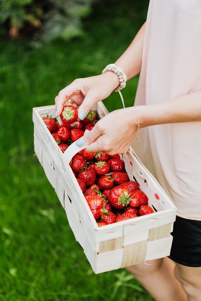 A person holding a wooden basket filled with ripe strawberries outdoors.