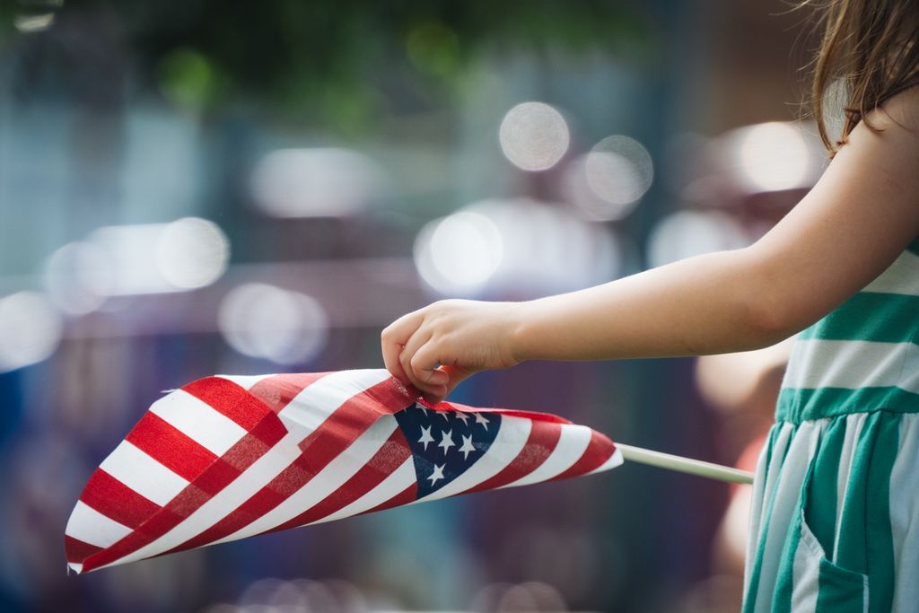 A young girl holding a small American flag outdoors, reflecting patriotism and joy.