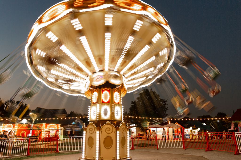 Blurred motion of an illuminated chain swing ride at a carnival during dusk.