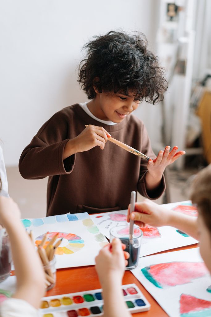 Happy child with curly hair painting with watercolors indoors. Creative and fun activity for kids.