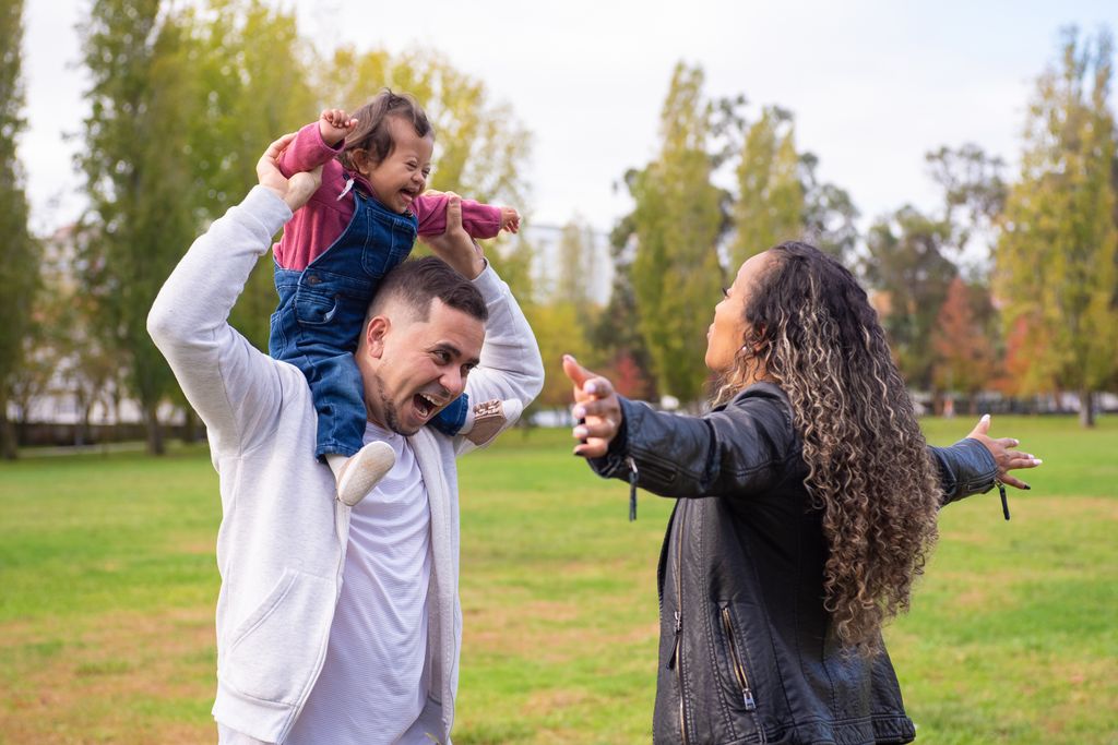 Happy family bonding outdoors with child on father's shoulders enjoying a day at the park.