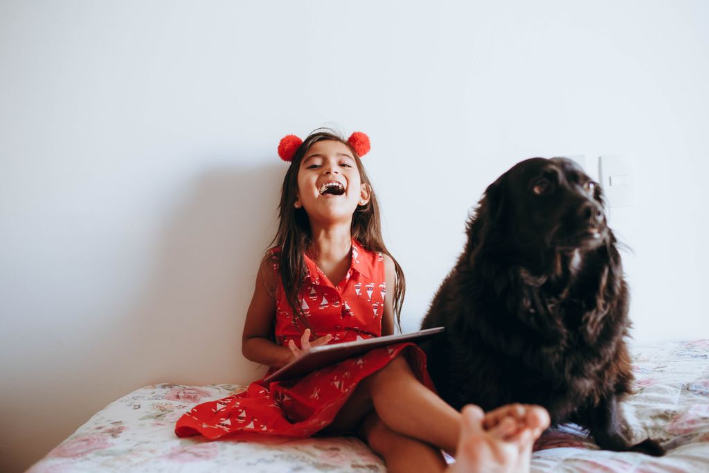 Joyful child in red dress laughing with a black dog indoors, capturing a heartwarming moment.