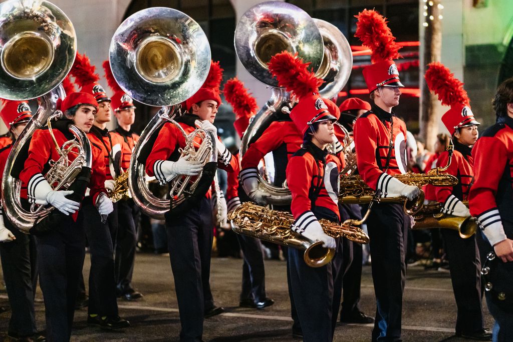 Marching band playing wind instruments during a night parade with vibrant red uniforms.