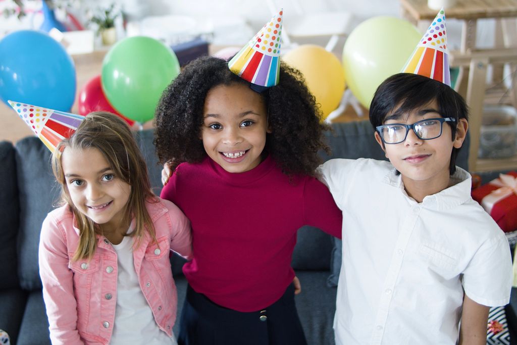Three kids smiling and celebrating a birthday with colorful balloons and hats indoors Roanoke, Va.
