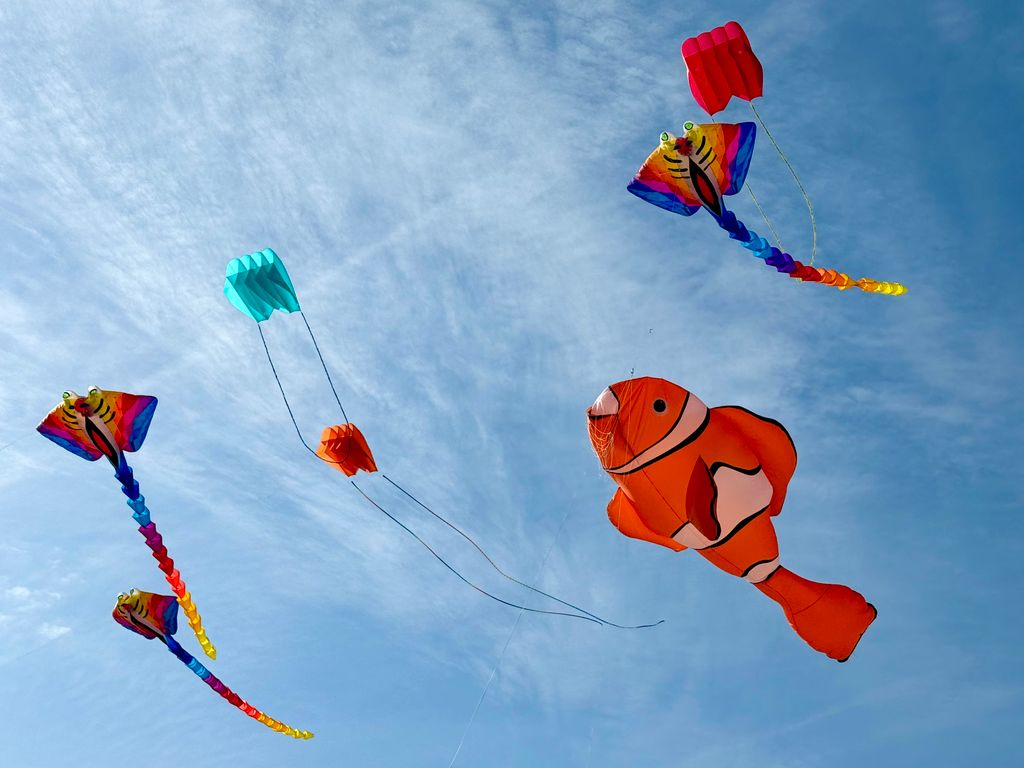 Vibrant animal-shaped kites soar against a clear blue sky at a kite festival.