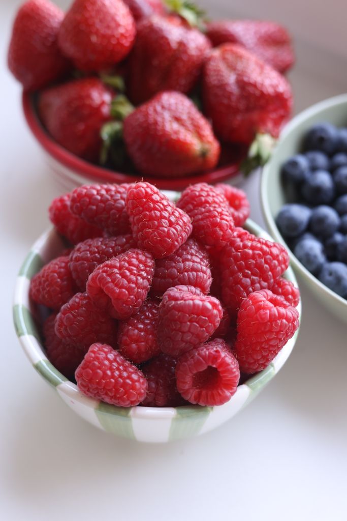 Vibrant display of raspberries, blueberries, and strawberries in white bowls, perfect for food photography.