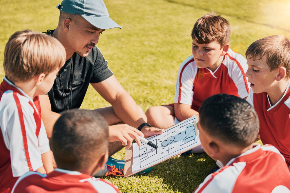 Kids sitting in a circle around a coach showing plays on a playboard.