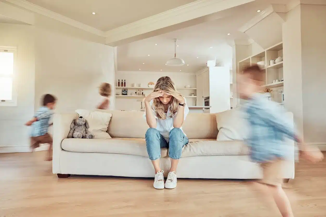 overwhelmed mom puts her head in her hands as kids run around